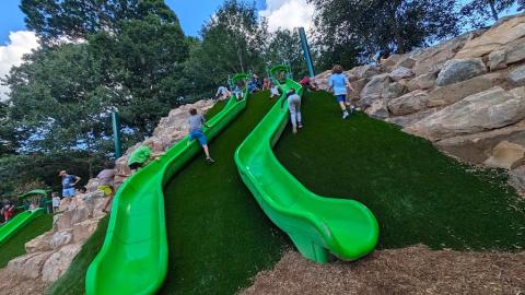 A huge new playground with green slides and many boulders on mulch under blue skies in Atlanta during a festival.