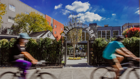 A photo of an old brick building wit a new gaming and restaurant concept inside with a small park outside next to a wide concrete pathway in Atlanta under blue skies.