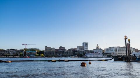 A view of Savannah Georgia on a river with many old buildings under blue sky.