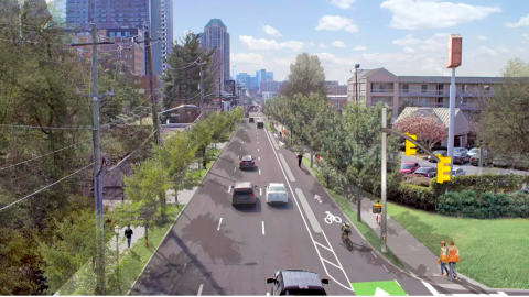 A wide street in Midtown Atlanta looking toward downtown with many people and cars on it, near lawns. 