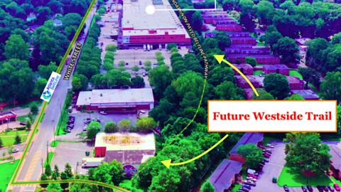 An aerial photo of a large trail site running between huge warehouse buildings and brick apartments.