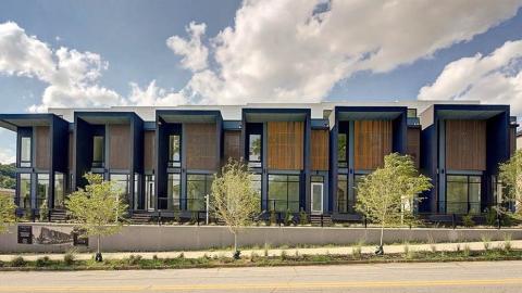 A row of modern townhomes with large windows and balconies under blue skies on a wide street with white modern interiors.