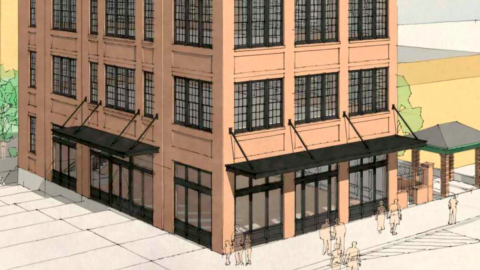 A site where a brick four-story corner building is planned to rise in Atlanta under blue skies next to two wide streets.