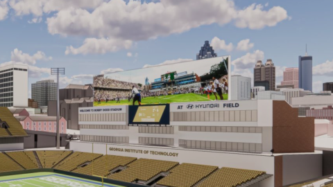 A large football stadium in the middle of a city under blue skies with many tall buildings and a big stadium with many seats in the middle. 