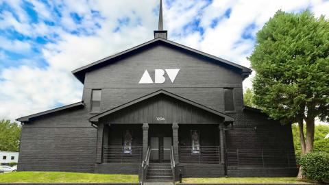 A photo of a large black church with white interiors and bright lights and many colorful paintings on the walls, with some stained glass retained.