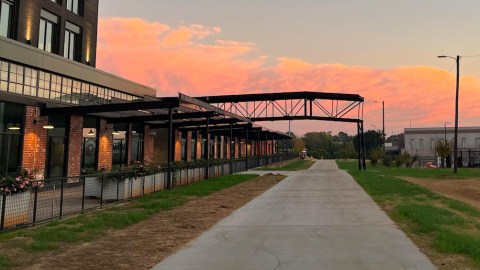 A photo of a long new concrete pathway shown beside old buildings and trees under a blue and pink evening sky.