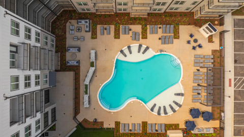 A photo showing a large new apartment complex with a pool in the middle and modern-rustic interiors north of Atlanta surrounded by woods and trees.