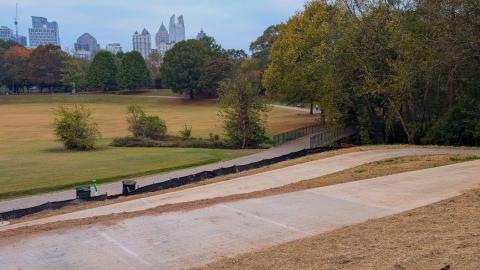 A photo of a long new concrete pathway shown beside trees and a huge park in Midtown Atlanta, Georgia.