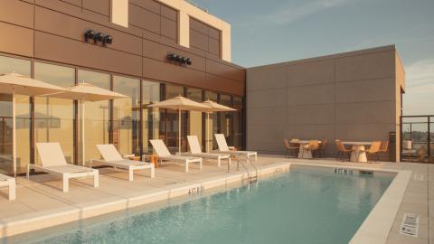 A photo of a new high-rise tower with a pool on top and modern-style white clad apartments inside with large windows.