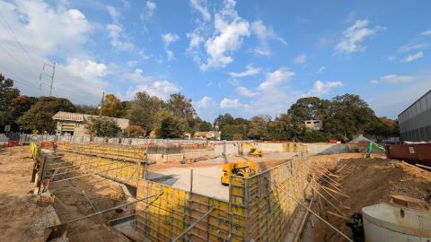 A photo of a construction site under blue skies with bulldozers and new concrete next to a large storage facility.