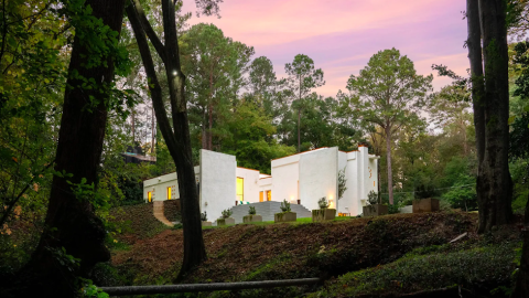 A large white stucco modernist dwelling on a big green property with airy white interiors surrounded by trees in the Buckhead area of Atlanta.