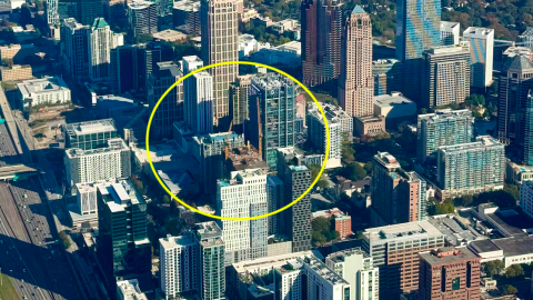 An aerial photo of a skyscraper project set among many glassy tall buildings near a wide freeway on a sunny morning in Atlanta Georgia.