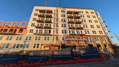 A photo of a large new apartment complex built with wood and with many balconies under construction cranes and blue skies.