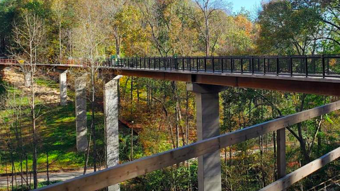 A photo showing a huge steel and concrete bike bridge next to yellow and red trees under blue skies in Buckhead Atlanta.