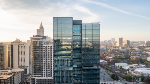 A photo of a large glassy new office high-rise building with huge floorplates situated next to a large freeway in Atlanta, near a forest of other tall buildings.