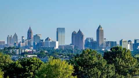 A photo of a skyline showing midtown and downtown Atlanta under blue skies near many trees.