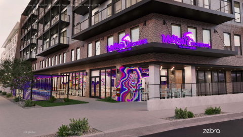 A photo of a colorful trippy and modern pizza joint with murals on the walls at the base of a large new apartment building with brick walls and balconies. 