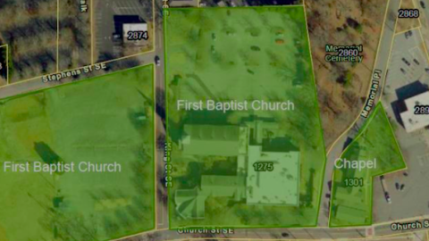 An overview of an old church near a downtown area with many large parking lots and wide roads nearby. 