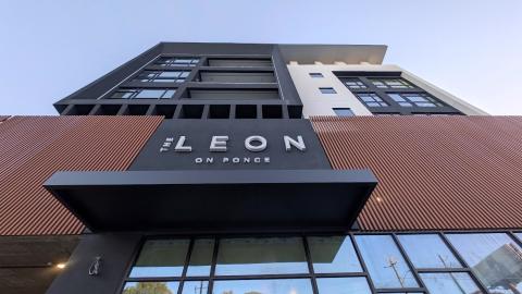 A photo of a large black white and brown modern condo building overlooking two wide streets and a carwash in Atlanta, under purple-blue skies, with modern interiors and tall ceilings.