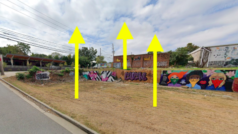 A vacant corner site of land and brick building under gray skies in Atlanta near a wide intown street.