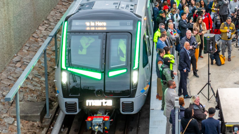 A photo of a sleek new MARTA train car with many people near it on tracks in a large Atlanta neighborhood.