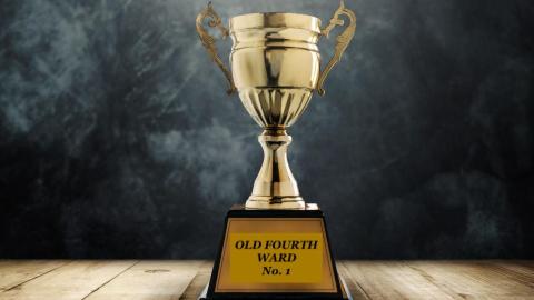 A photo of a golden trophy with a black backdrop and wood at its base. 