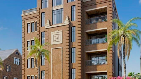 An image of a large ornate condo building and townhome site in downtown Savannah under blue skies next to a large river.