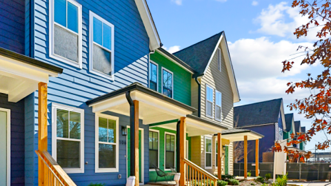 A photo of a row of modern houses with white interiors under a blue sky near a sidewalk and colorful trees in Atlanta. 