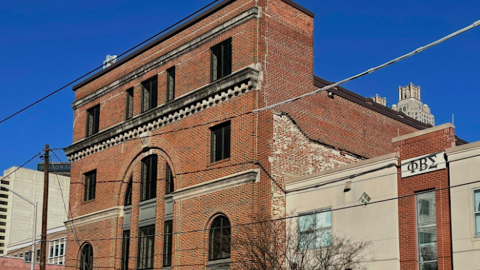 A photo of a large brick building under blue skies front a wide street near many tall buildings in downtown Atlanta.