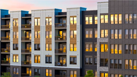 A rendering of a mid-rise new apartment complex under blue skies with many windows, a large pool at the center, and big gym, with new modern apartments with white walls. 