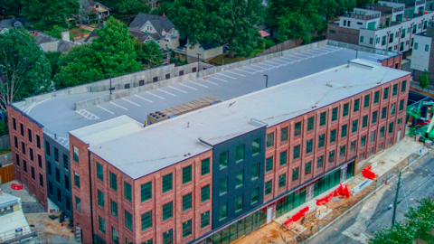 An aerial image showing a large brick and concrete building between large houses and a wide street.