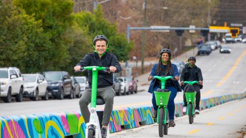 A photo of a people riding escooters and bikes in Atlanta under gray skies, all wearing helmets.