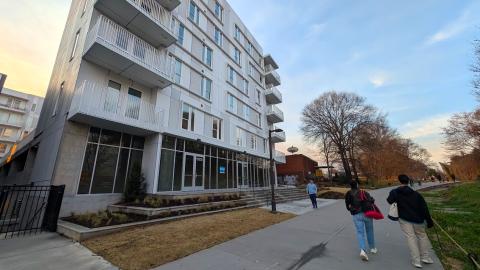 A photo of a large white building that stand over a wide concrete trail and streets in Atlanta with stacked apartments and spaces for shops and retail. 