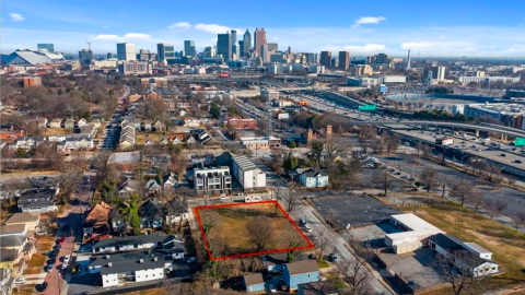 An aerial view of site planned for townhomes four stories tall with roof decks just south of many skyscrapers and near a wide highway.