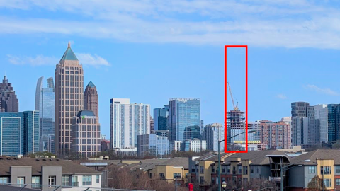 A photo of a large new skyscraper under construction under blue skies in Midtown Atlanta surrounded by many other buildings and wide streets.