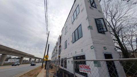 A photo of a three-story building wrapped in white installation under construction in Atlanta Georgia near an elevated rail line and wide street.