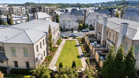 A photo of a row of stone and brick townhomes in a suburban setting under blue skies with green lawns.