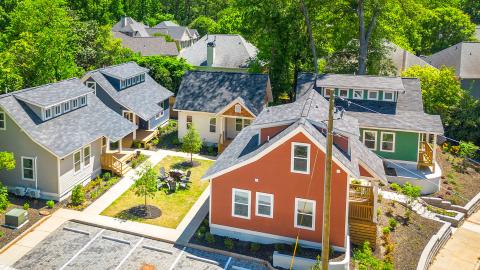 An overview of a colorful small home community near a parking lot and wide street and many trees.