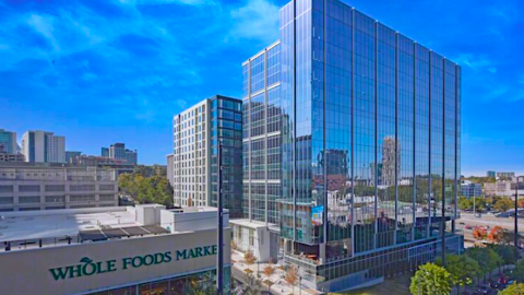 An image of a newer tall glassy office building near wide streets with modern white interiors in the making under blue skies in Atlanta. 