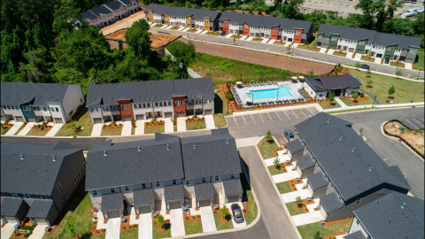 A photo of a large new townhome community with a pool at its center and many colorful facades near trees and homes with modern white interiors.