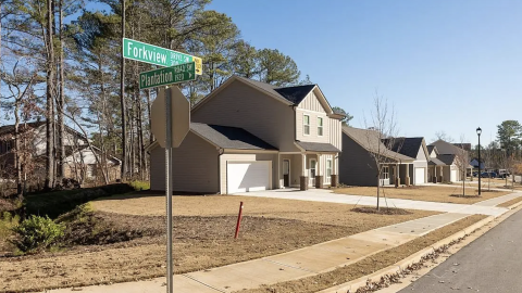 A photo of a subdivision with new housing and homes with front-facing garages under blue skies near many trees in suburban Atlanta.