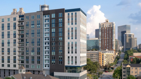 A photo of a large white gray and black building over a large park in downtown Atlanta under blue skies.