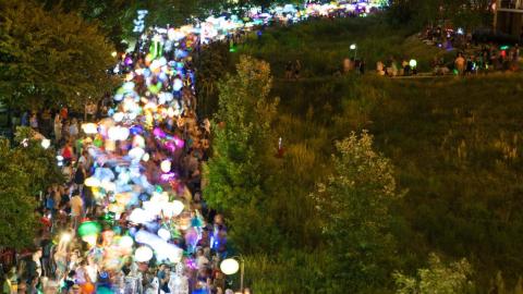 A huge row of people with illuminated lanterns walking between trees and bushes in Atlanta.