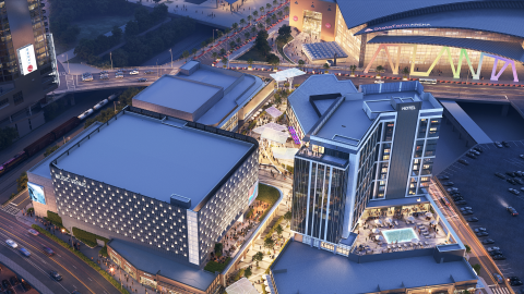 An overview of a large new development at night with many shorter buildings and a long lighted section near big stadiums and railroad tracks.