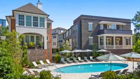 A new community of townhomes and large houses under blue skies with a saltwater pool in front.