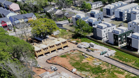 Image showing a large new project next to many new white homes and multicolored homes in a field near a wide street in Atlanta.