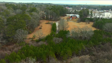 An overview of a large vacant lot site near many homes and trees in south Atlanta near wide street and a shipping facility.