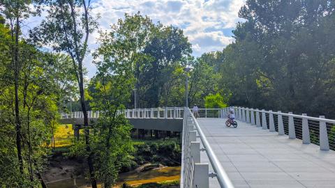 An image of a long bike and pedestrian trail in Atlanta near many trees and a large creek and numerous intown cities. 