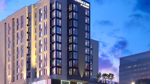 A rendering of a large gray hotel under purple skies in downtown Atlanta near a large park and wide streets.