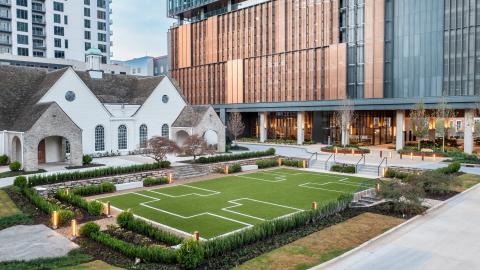 An image of a large new glassy office building and a small greenspace with a white older building beside it in downtown Atlanta with a lot of new lighting. 